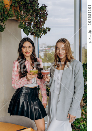 Attractive women are clinking and toasting with cocktails in restaurant or bar while looks camera Attractive women are clinking and toasting with cocktails in restaurant or bar while looks camera 108681101