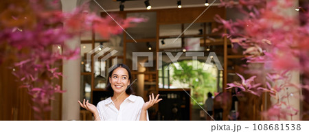 Vertical shot of enthusiastic brunette girl looking excited, raising hands up, posing near cafe entrance, inviting people to her restaurant 108681538