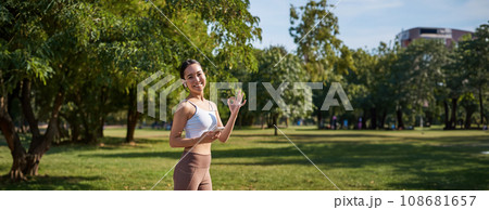 Sport and wellbeing. Young sportswoman in park, listen music and smiling, workout outdoors, jogging on streets of city 108681657