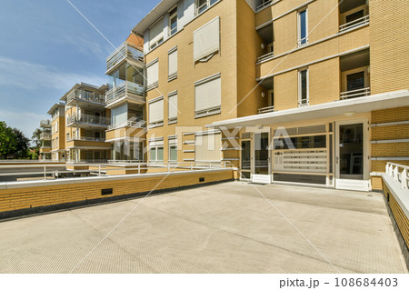 an outside area with some buildings in the background and a white fence on the other side of the building there is a blue sky an outside area with some buildings in the background and a white fence on the other side of the building there is a blue sky 108684403