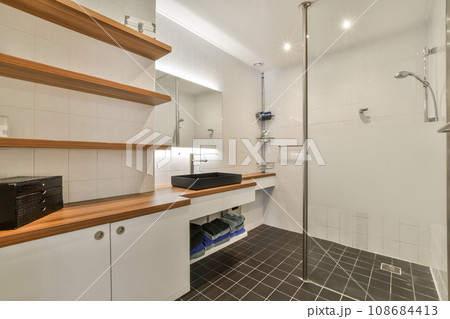 a bathroom with white tiles and wooden shelves on the wall, along with a glass shower stall in the corner a bathroom with white tiles and wooden shelves on the wall, along with a glass shower stall in the corner 108684413