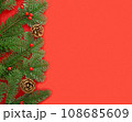 Green fir branches with red berries and brown cones on the left on the red background. 108685609