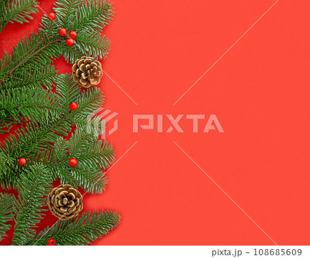 Green fir branches with red berries and brown cones on the left on the red background. 108685609