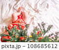 Newborn baby in red clothes located under the decorated christmas tree. 108685612