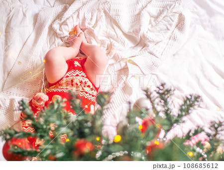 Newborn baby in red clothes located under the decorated christmas tree. 108685612
