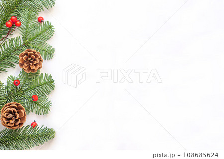 Green branches with red berries and brown cones to the left on white background. 108685624