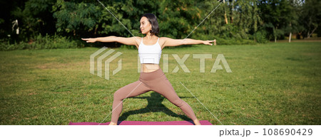 Young woman stretching her body, workout and doing yoga in park, standing on rubber mat in fitness clothing during training session Young woman stretching her body, workout and doing yoga in park, standing on rubber mat in fitness clothing during training session 108690429