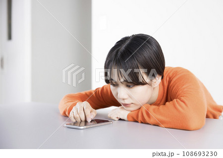 机にあごを乗せスマホを見る若い女性 108693230