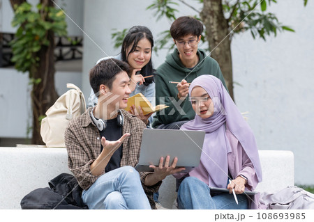 Multiracial smiling group of teenage student using laptop doing homework and enjoying a relaxed atmosphere outdoors at the university campus. Education concept. High quality photo Multiracial smiling group of teenage student using laptop doing homework and enjoying a relaxed atmosphere outdoors at the university campus. Education concept. High quality photo 108693985