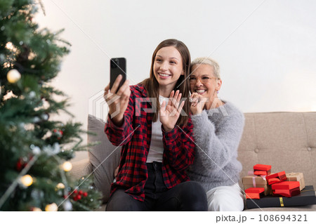 Cheerful daughter and mother celebrate christmas at home and with friend and family through a video call Cheerful daughter and mother celebrate christmas at home and with friend and family through a video call 108694321