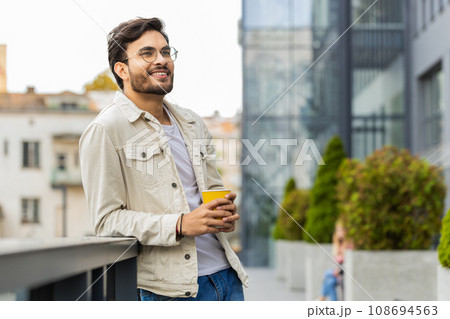 Happy Indian man enjoying drinking morning coffee hot drink, relaxing, taking a break in city street 108694563