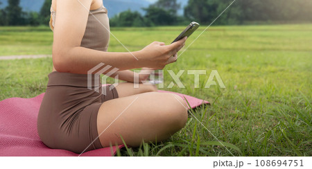 Woman asian looking at her smartphone and reading on look sport application at the park Woman asian looking at her smartphone and reading on look sport application at the park 108694751
