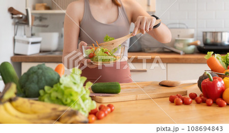 Young woman standing in the kitchen making a salad for health Young woman standing in the kitchen making a salad for health 108694843