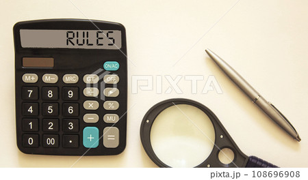 Calculator with the text RULES on a white background with a magnifying glass and a pen nearby Calculator with the text RULES on a white background with a magnifying glass and a pen nearby 108696908