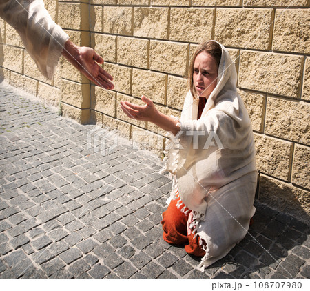 A girl in poor clothes sits on the ground 108707980
