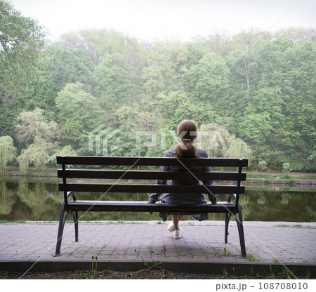 Lonely girl on a bench by the lake Lonely girl on a bench by the lake 108708010