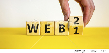 WEB 1 or 2 symbol. Businessman turns a wooden cube and changes words WEB 1 to WEB 2. Beautiful yellow table, white background, copy space. Business, technology and WEB 1 or 2 concept. 108708347