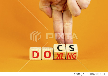 Docs or doxing symbol. Concept words Docs Doxing on wooden block. Beautiful orange table orange background. Businessman hand. Business docs or doxing concept. Copy space. Docs or doxing symbol. Concept words Docs Doxing on wooden block. Beautiful orange table orange background. Businessman hand. Business docs or doxing concept. Copy space. 108708384