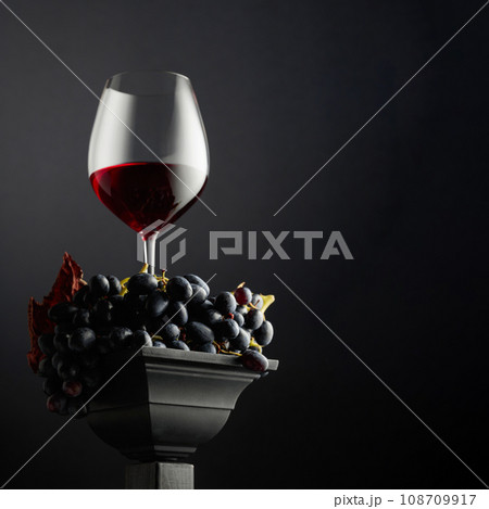 Blue grapes and a glass of red wine on a black background. 108709917