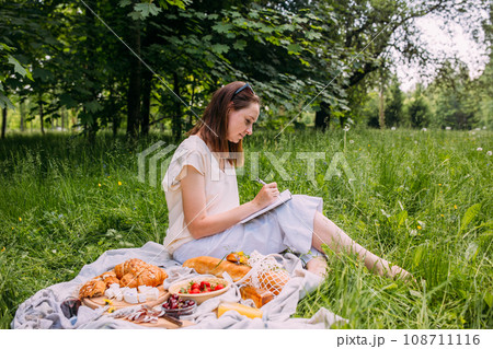 Beautiful woman on picnic. She smiles, eats strawberries and enjoys summer. Beautiful woman on picnic. She smiles, eats strawberries and enjoys summer. 108711116