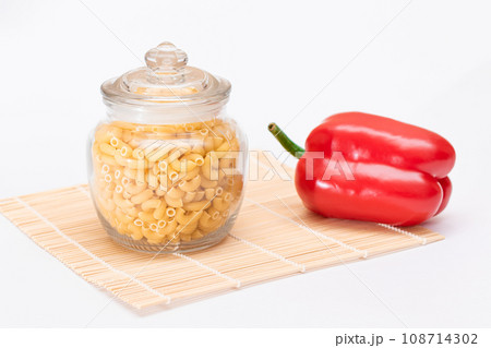 Uncooked Chifferi Rigati Pasta in Glass Jar and Red Bell Pepper on Bamboo Mat Isolated Uncooked Chifferi Rigati Pasta in Glass Jar and Red Bell Pepper on Bamboo Mat Isolated 108714302
