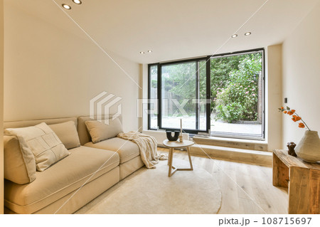 a living room with a couch, coffee table and large window looking out onto the backyard garden in the background 108715697
