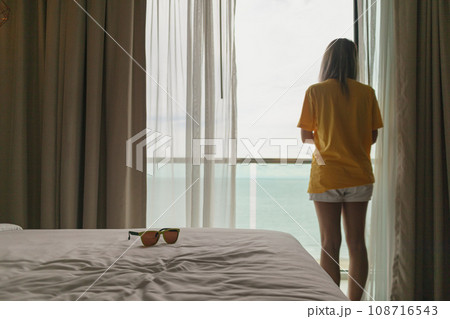 Woman standing at the balcony by the curtain looking out to the sea in vacation. Woman standing at the balcony by the curtain looking out to the sea in vacation. 108716543