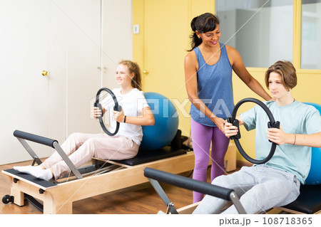 Pilates instructor helps teenager do exercises with ring Pilates instructor helps teenager do exercises with ring 108718365