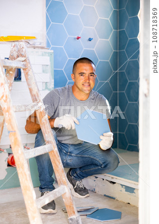 Cheerful man setting tile in bathroom Cheerful man setting tile in bathroom 108718369