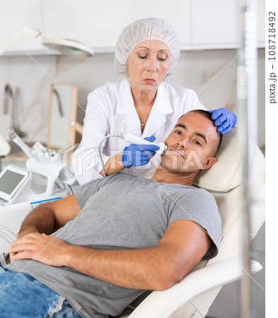 Female cosmetologist performing anti-aging face phototherapy procedure for male client in clinic of aesthetic clinic 108718492