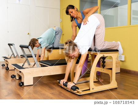 Pilates instructor helping gyrl doing exercises on reformer apparatus at gym 108718543