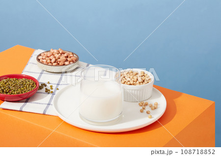 Soybeans, peanuts and green beans are contained inside dishes and a bowl. Glass cup filled with nut milk. Different types of nuts may have slightly different micronutrient 108718852