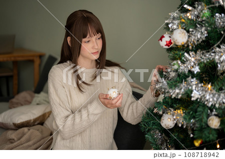 A happy woman is enjoying decorating a Christmas tree and celebrating Christmas holiday at home. A happy woman is enjoying decorating a Christmas tree and celebrating Christmas holiday at home. 108718942
