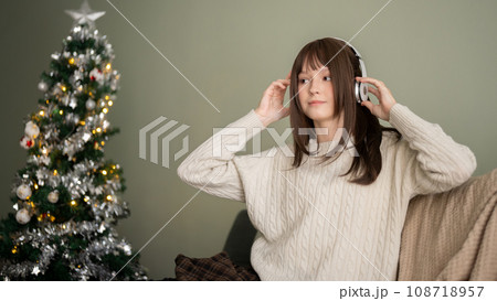 A happy woman is enjoying Christmas playlist through her headphones, celebrating Christmas at home. 108718957