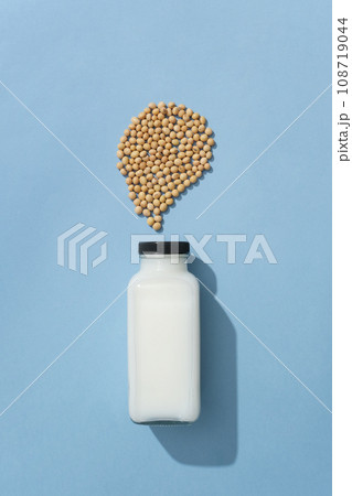 Unlabeled glass bottle of fresh milk decorated on blue background with a handful of soybeans. Soybeans can help maintain the elasticity of our skin Unlabeled glass bottle of fresh milk decorated on blue background with a handful of soybeans. Soybeans can help maintain the elasticity of our skin 108719044