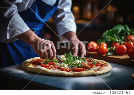 Closeup hand of chef baker in uniform blue apron cutting pizza at kitchen. Or makes the final touches to the preparation of pizza. Sprinkles it with parmesan cheese Closeup hand of chef baker in uniform blue apron cutting pizza at kitchen. Or makes the final touches to the preparation of pizza. Sprinkles it with parmesan cheese 108721468