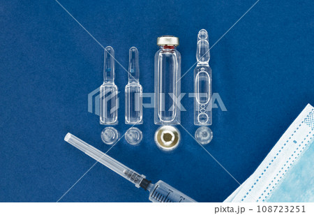 Blank vaccine vial, medical mask and syringe on blue background with copy space, top view. 108723251