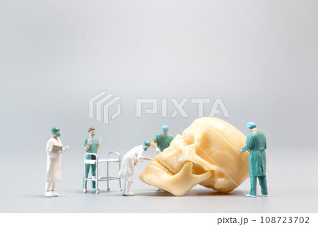Miniature people Doctor with a giant human skull on a grey background 108723702