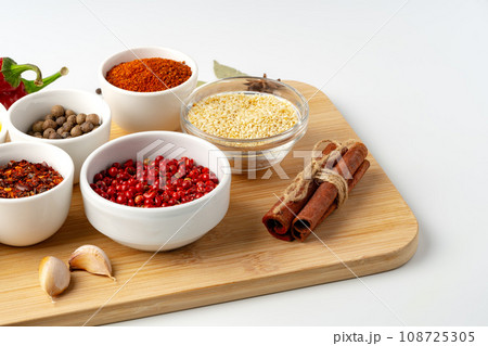 Bowls with spices on wooden board on white background Bowls with spices on wooden board on white background 108725305