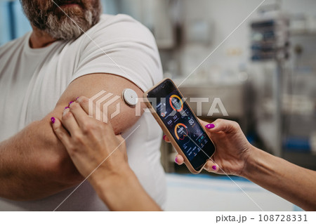 Doctor connecting continuous glucose monitor with smartphone, to check blood sugar level in real time. Obese, overweight man is at risk of developing type 2 diabetes. Concept of health risks of Doctor connecting continuous glucose monitor with smartphone, to check blood sugar level in real time. Obese, overweight man is at risk of developing type 2 diabetes. Concept of health risks of 108728331