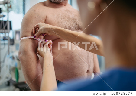 Female doctor measuring arm circumference of overweight patient using tape measure. Obesity affecting middle-aged men's health. Concept of health risks of overwight and obesity. 108728377