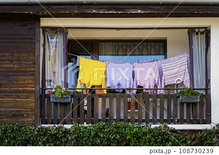 Colorful clothes drying on a balcony, hanging from washing line, front of old wooden house facade Colorful clothes drying on a balcony, hanging from washing line, front of old wooden house facade 108730239