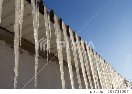 Sharp icicles and melted snow hanging from the eaves of the roof. Beautiful transparent icicles slowly gliding of a roof Sharp icicles and melted snow hanging from the eaves of the roof. Beautiful transparent icicles slowly gliding of a roof 108731007
