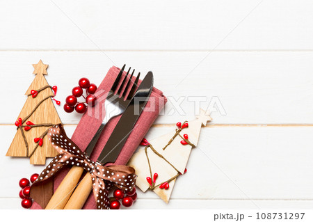 Top view of fork and knife tied up with ribbon on napkin on wooden background. Christmas decorations and New Year tree. Happy holiday concept with empty space for your design 108731297