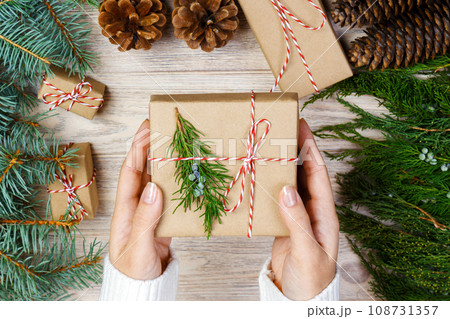 Christmas gift wrapping background. Female hands packaging christmas present wrapped in kraft paper top view. Winter holidays concept flat lay Woman holding Christmas gift box Christmas gift wrapping background. Female hands packaging christmas present wrapped in kraft paper top view. Winter holidays concept flat lay Woman holding Christmas gift box 108731357