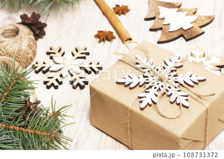 Christmas background with gift boxes wrapped in kraft paper, fir tree branches, pine cones, cinnamon sticks and stars anise on white wooden background 108731372