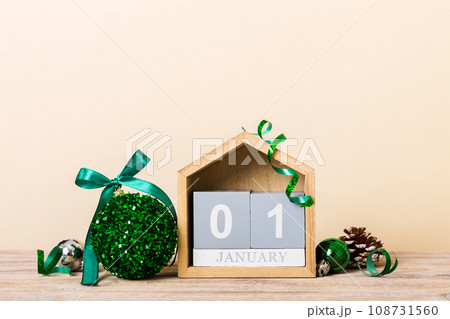 1 january. Christmas composition on colored background with a wooden calendar, with a gift box, toys, bauble copy space 108731560