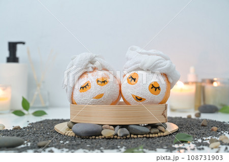 Orange fruits in face mask, zen stones, candles and green leaves on white background. Spa treatment and self care concept 108731903