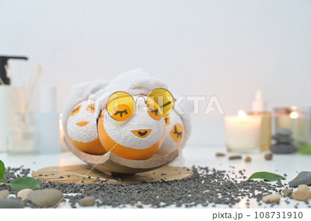 Orange fruits in face mask, zen stones, candles and green leaves on white background. Spa treatment and self care concept Orange fruits in face mask, zen stones, candles and green leaves on white background. Spa treatment and self care concept 108731910