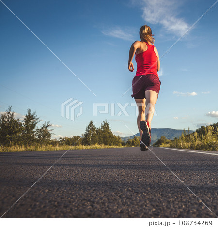 Fitness blonde woman running on the asphalt road at the mountains 108734269